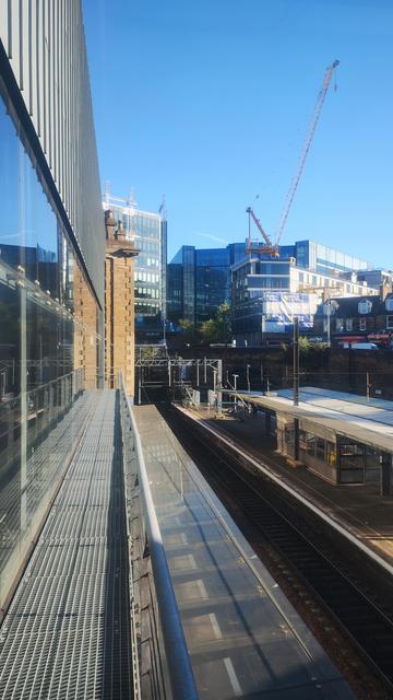 View out the windows of the bridge over the tracks at Haymarket Station, showing the edge of the building, the tracks below, a modern, tall building in the distance