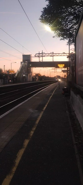 Looking along a train platform with sunset skies in the background, as an express train appears and hurtles through the station and gone