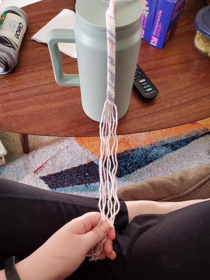 View down my lap, where my white hands are holding strands of yarn from where they're secured on my water tumbler. I'm sitting cross legged on my couch.