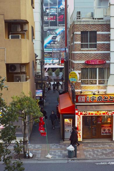Narrow alley between two buildings. Perspective from an elevated platform. Colourful signs.