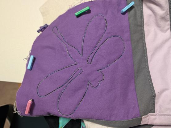 A big dragonfly in shiny green-to-blue variegated thread on a purple square, forming the corner of a quilt.