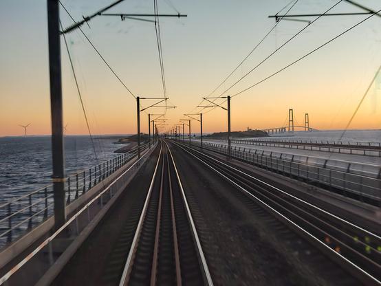 View out the rear of an IC3 train.
The Great Belt bridge in the horizon, with the sun rising behind it.
