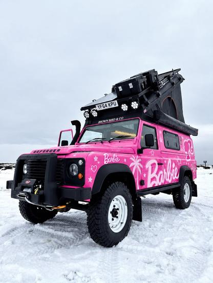 An off grid Defender camper van, in bright pink, with Barbie printed on the side