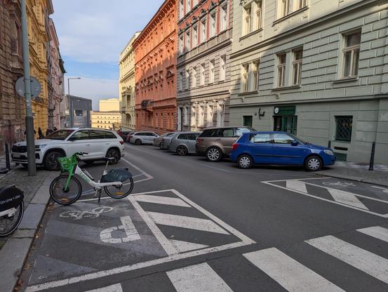 Residential street with cars parked diagonally on both sides. A small zone of a couple square meters is reserved for bicycle parking next to the pedestrian crossing, without anything to attach a bike. It's basically only used to keep the free-floating bicycles out of the way.