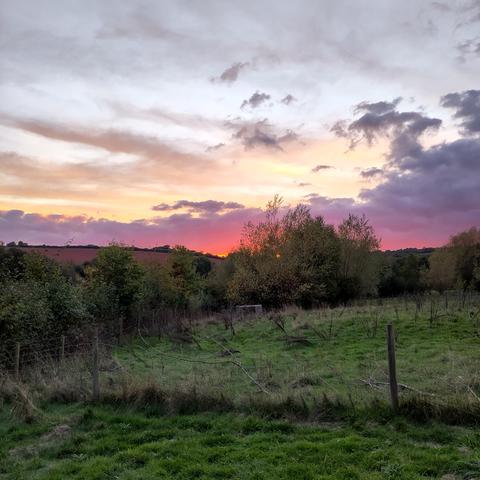 Sunset over Exmoor, lilac cloud over a peach and gold sky, shading to fuschia pink and tangerine on the horizon
