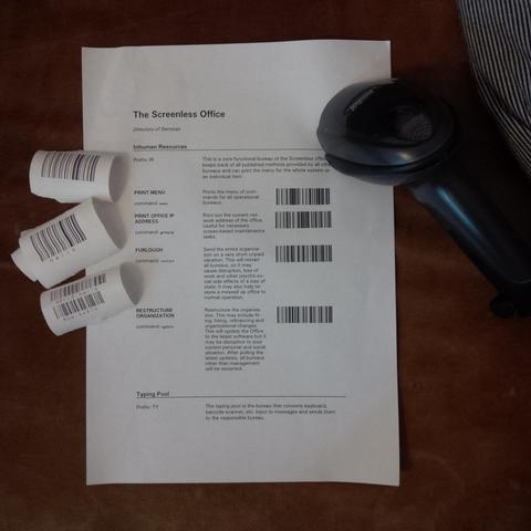 Some bits of receipt printer paper with barcodes printed on them. A barcode scanner. A sheet of paper that says "The Screenless Office" with a table describing the functions of the "Inhuman Resources" department.