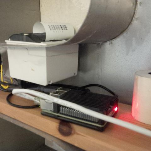 An inner view of the metal housing. There's a Raspberry Pi, some messy cables and the inside of the receipt printer.