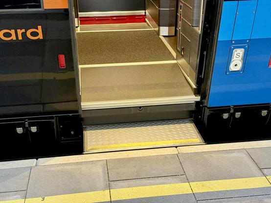 Detailed view of the lower part of a train entrance door. There is a movable step at platform level but then there is a step if maybe twenty centimetres into the carriage.