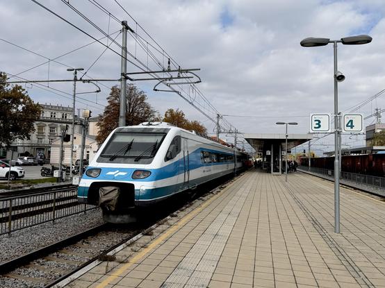 A boxy pendolino train in white and blue waiting on a platform.