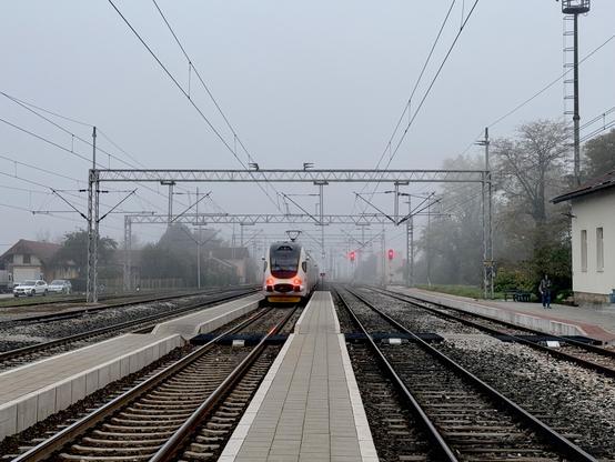 An electric train is leaving from a very low, very narrow platform between tracks into a foggy distance.