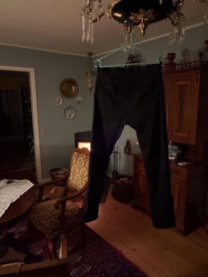 Trousers hanging from a small chandelier in a room of antique furniture and a modern wood burner.