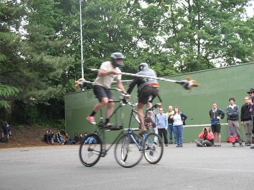 Two people on tall bikes joust with each other