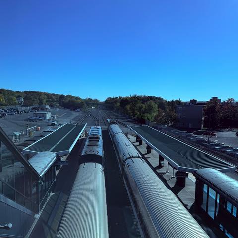 Two trains are parked at a railway station with platforms on either side under a clear blue sky.