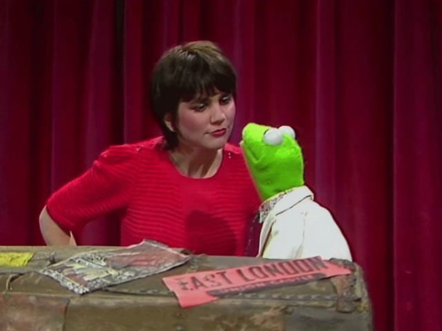 GIF of Kermit the Frog attempting to kiss Linda Ronstadt only for Miss Piggy to punch her way out of a locked trunk, startling both Kermit and Linda