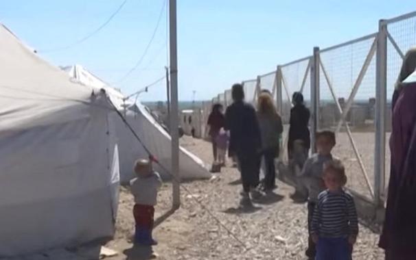 Des enfants et des adultes derrière les grilles d’un camp.
