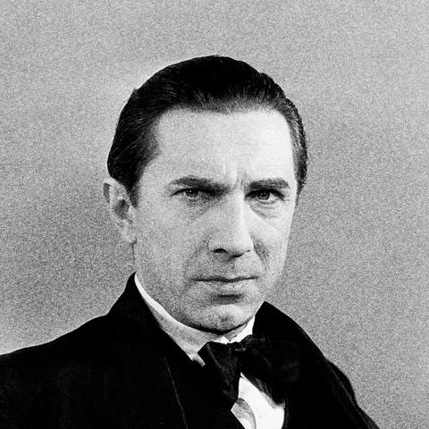 A grainy black and white photograph of Bela Lugosi, in a black coat with a black bow tie and white shirt. He looks directly at the camera with a serious yet inscrutable expression.