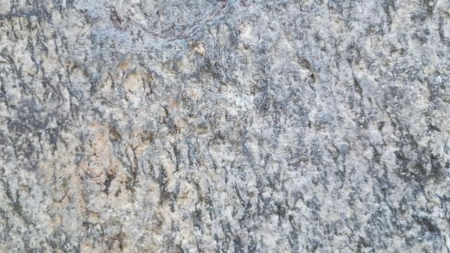 Closeup of a rough-hewn stone in a stone wall, mostly light gray with darker flecks.