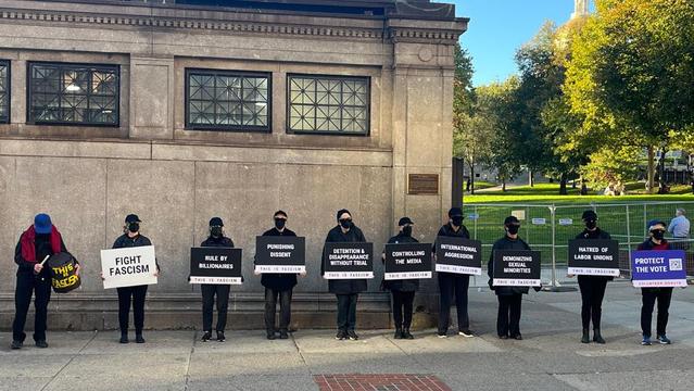 Black-clad, black-masked people holding signs against fascism outside Park Street MBTA station