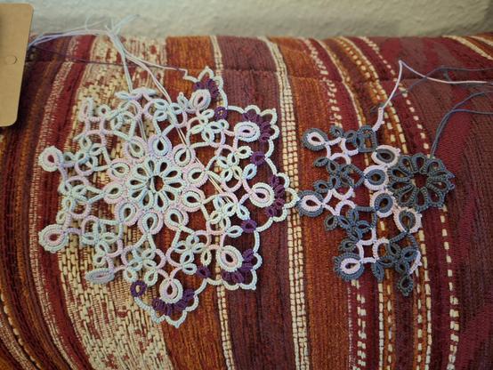 Two incomplete doilies, one in pink and purple yarn with a very light icy gray for contrast, and the other with the same pink and a slate gray / anthracite for contrast.