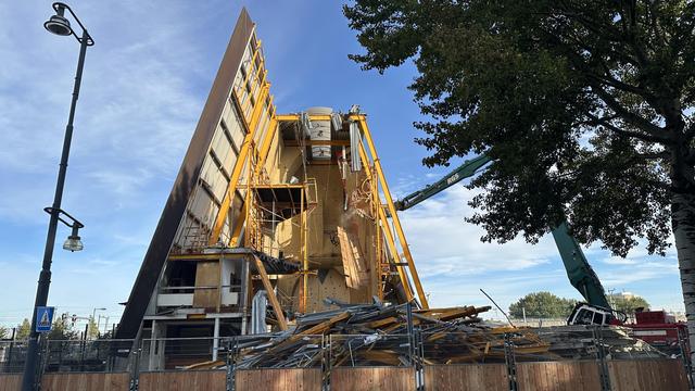 Tall building being demolished. A large wooden panel is falling to the ground inside.