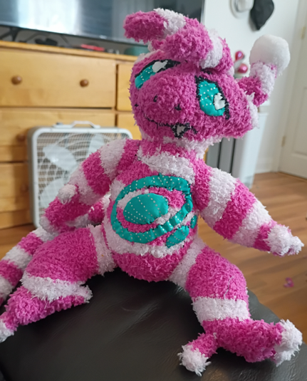 an irl sock plush of the character "stretch" from Space Case, a pink, alien-looking electabuzz