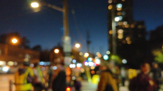 Photo of cyclists, many with fluorescent safety gear, gathering in a parking lot near Bloor and Islington just after sunset. Blurred for privacy.