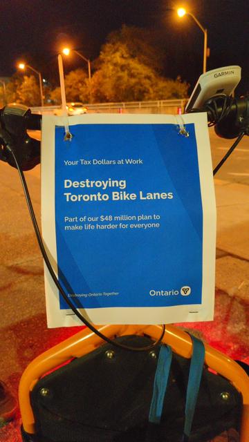 On the front of a cargo bike, a poster made to look like official Ontario ones, reading "Your Tax Dollars At Work
Destroying Toronto Bike Lanes
Part of our $48 million plan to make life harder for everyone"
And in small print: "Destroying Ontario Together" and the Ontario trillium logo.