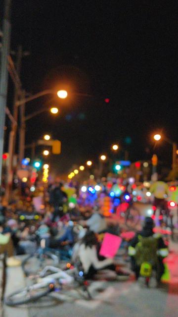 The bike lane along Bloor full of cyclists lying on the ground with their bikes. Bike cops are starting to move in along the road side. Blurred for privacy.