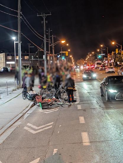 A crowd of cyclists at night laying in bike lanes, spreading out into the distance, surrounded by construction pylons and signs.