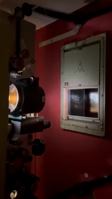 Close up video of a 35mm projector with a camera pan towards the window where you can see parts of the film being projected