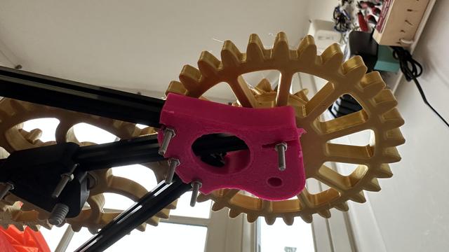 Underside of a clockwork mechanism with a hot pink shape bolted to it.