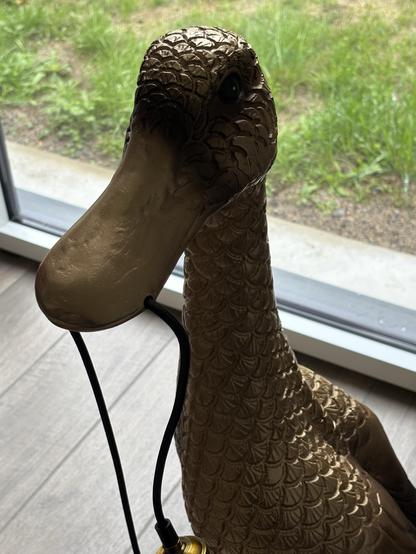 La lampe canard avec sa tête et son bec qui tient le fil vue de près.