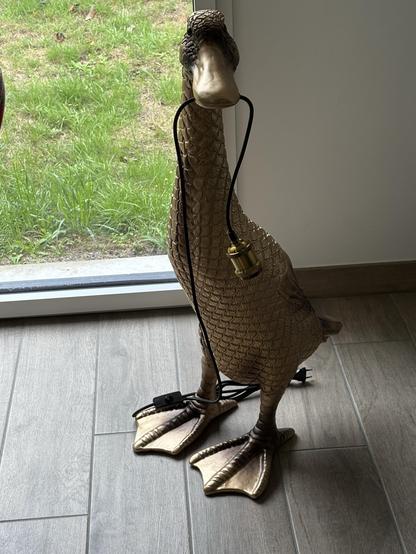La magnifique lampe canard sur pied, couleur doree. Le canard tient le fil dans son bec.