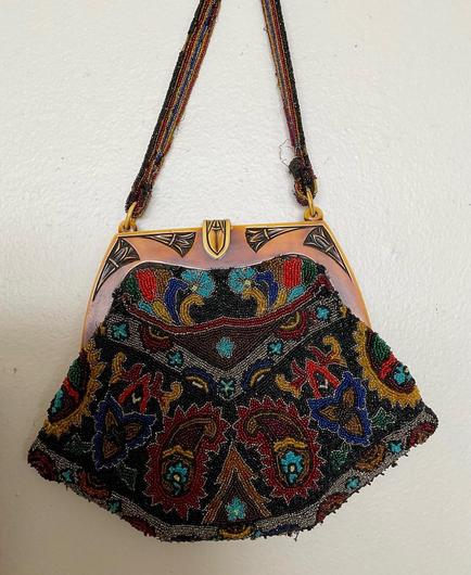 A fully beaded bag with very small beads in dark jewel tones of navy blue, wine red, turquoise, and gold. Art Nouveau Persian style paisley floral motif, with art nouveau tortoiseshell Bakelite sculpted clasp. It used to have a looping fringe at the bottom, but it fell apart and I removed it.