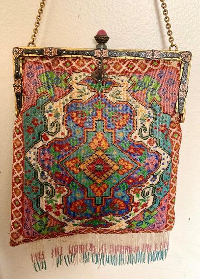 A very finely beaded bag with fringe at the bottom in pink green blue beige and gold. The pattern is a Persian medallion rug style design. The closure is in gold ormolu with a silvery cloisonee swirl and knot design layered on top inset with tiny faceted jet beads. The clasp is an egg shaped rose quartz? stone and looks like a deep pink egg in a (unknown metal) cup. It has a small metal jewel like tassel with jet beads hanging from the clasp. The photo does not do the jet inlay justice and how it sparkles when it catches the light.