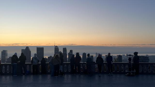 A group of people, silhouetted against the sunrise skyline of Montreal from Mount Royal