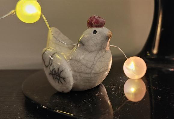 A small white raku ceramic chicken from moonrabbit, sitting on a monitor stand with two small coloured illuminated balls by her side.