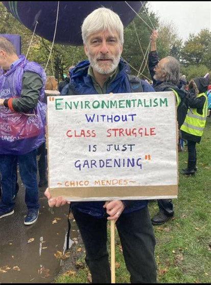 there is a random white dude, holding a banner saying: "Environmentalism without class struggle is just gardening" - Chico Mendes