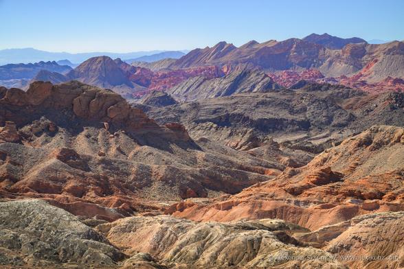 Color landscape photo of a barren desert landscape with many intersecting ridges of different geologic origin, all under a clear blue sky and in direct sunlight.