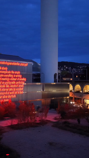 Evening drone shot of the neon LED installation «HowToSabotageWorkBetter_2027.pdf»