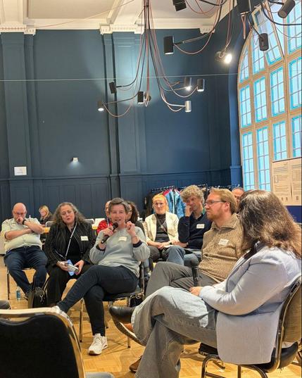 Teilnehmende des Dialogs für Cybersicherheit in einer Fishbowl-Diskussion. Eine Frau spricht in ein Mikrofon, Teilnehmende hören interessiert zu.
