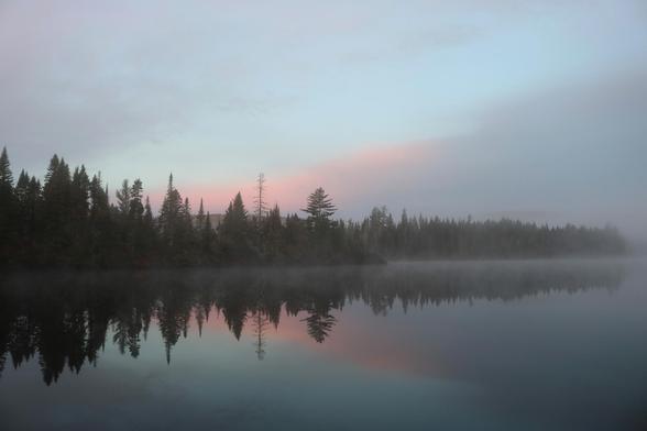 Photograph of an autumn landscape showing a completely calm lake at sunrise. Large conifers grow on the opposite shore and reflect in the lake, just like the blue sky with purple and pink clouds. A slight mist floats on the surface of the lake.

Photographie d'un paysage automnal montrant un lac complètement calme au lever du soleil. De grands conifères poussent sur la rive opposée et se reflètent dans le lac, tout comme le ciel bleu avec des nuages mauves et roses. Une légère brume flotte à la surface du lac.