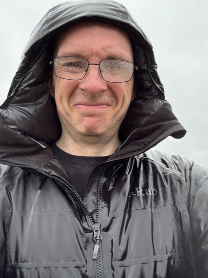 A selfie (of me, obviously) in a jacket with the hood up, noticeably wet, glasses steamed up and a grimace on my face.