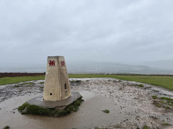 The point at the top of the Garth, surrounded in a puddle, looking out on the rain-soaked valleys.

The point has a Welsh dragon painted on it.