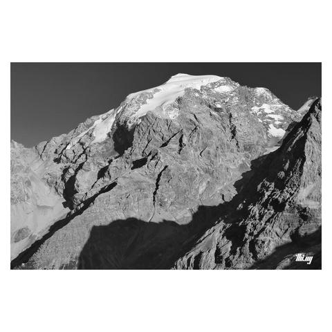 B&W photo of the Ortler mountain (3905m) with a long major ridge running down diagonally into the valley. A tiny looking mountain hut in bottom-left corner (itself still 600 meters above the valley). A glacial side valley in between another ridge in the front, the ice already mostly retreated and only remaining near the top. High contrast light from the bright October afternoon sun. Clear dark sky.