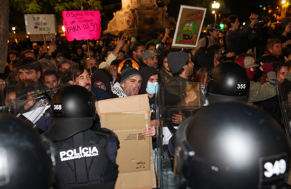 A protestor holding a piece of cardboard in front of riot police.