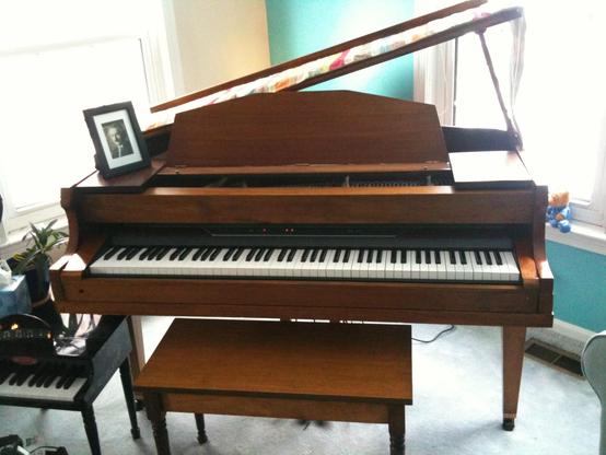 A baby grand piano where the action has been replaced with a digital unit.
