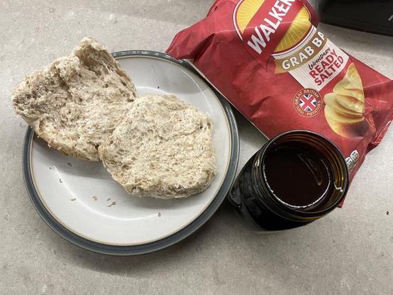 a plate with a roll on it, next to a new jar of marmite and some walkers ready salted