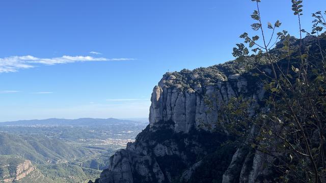 The sharp edge of the Montserrat mountain juts out against a blue sky near the top, with the river valley to Barcelona stretching out below