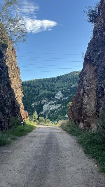 Two sides of a canyon glow around the gravel road they frame, with a tall hill stretching out in the background under a blue sky in Catalonia south of Montserrat
